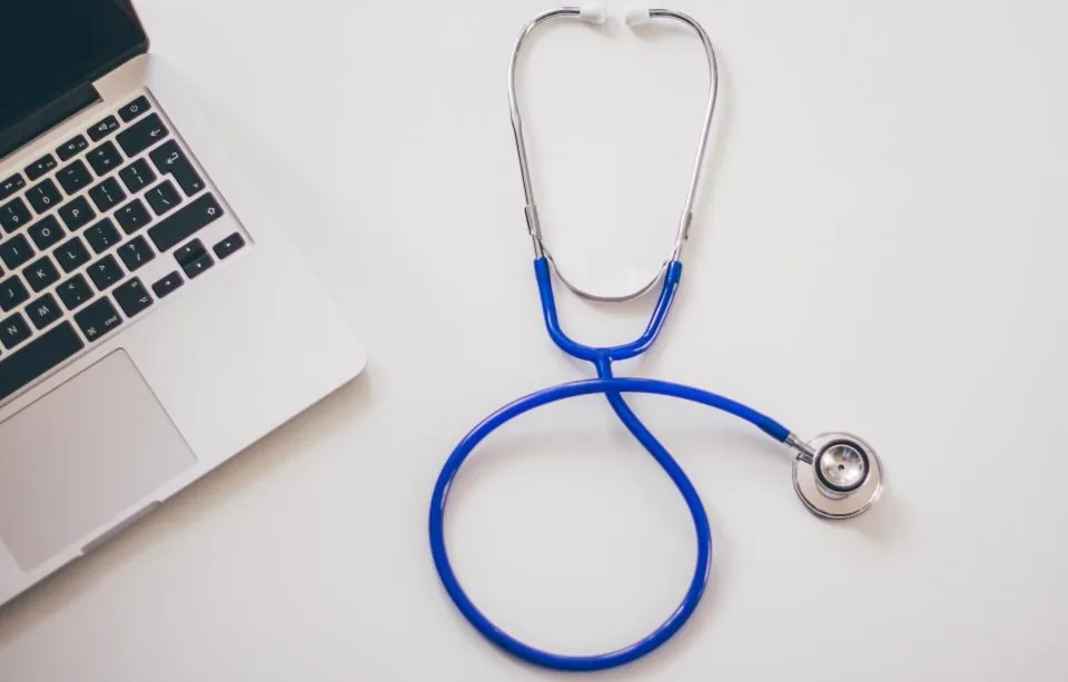 A stethoscope resting on a desk beside a laptop